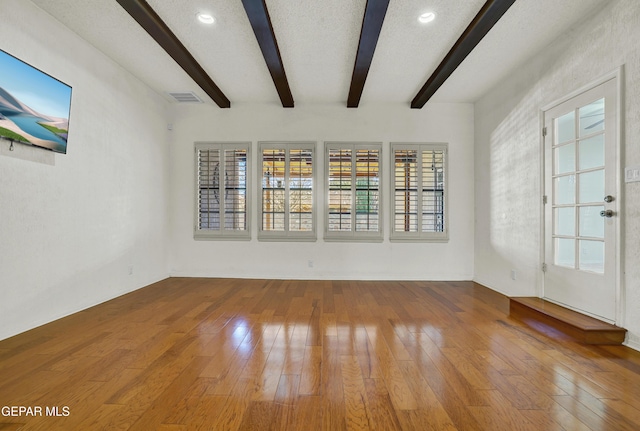 empty room featuring beamed ceiling, wood-type flooring, and a textured ceiling