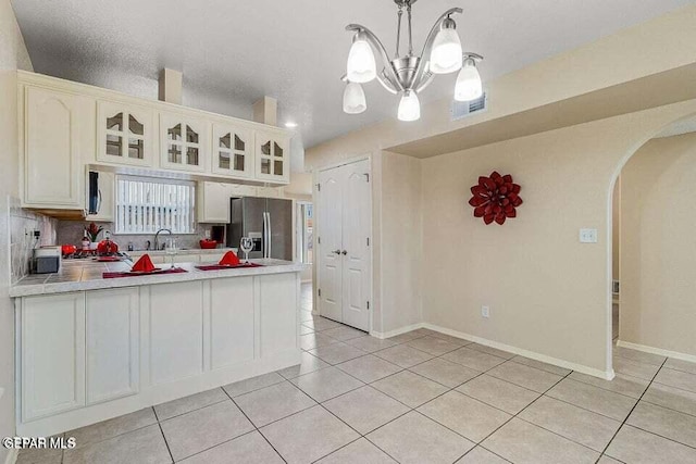 kitchen with light tile patterned flooring, stainless steel fridge with ice dispenser, hanging light fixtures, and white cabinets