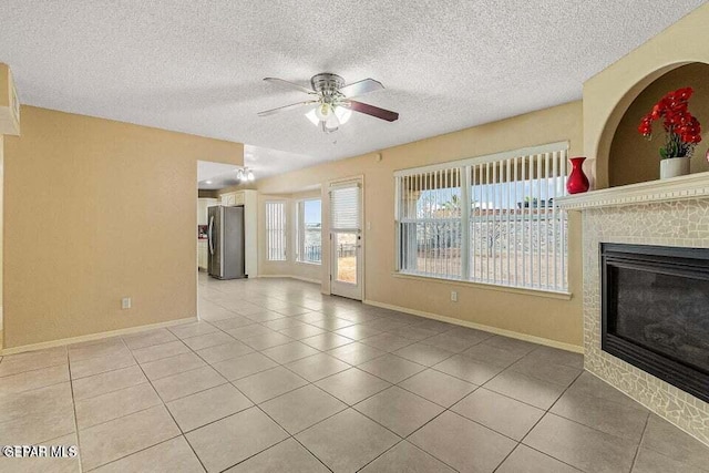 unfurnished living room featuring ceiling fan, a tiled fireplace, a textured ceiling, and light tile patterned floors