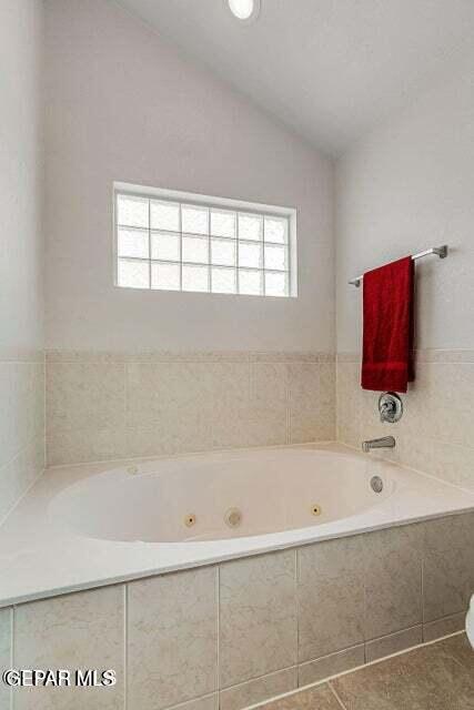 bathroom with a relaxing tiled tub, tile patterned floors, and vaulted ceiling