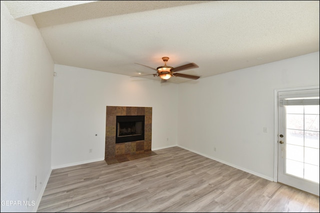 unfurnished living room with ceiling fan, a tiled fireplace, light hardwood / wood-style floors, and a textured ceiling