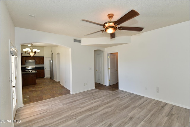 empty room featuring ceiling fan with notable chandelier, a textured ceiling, and light wood-type flooring