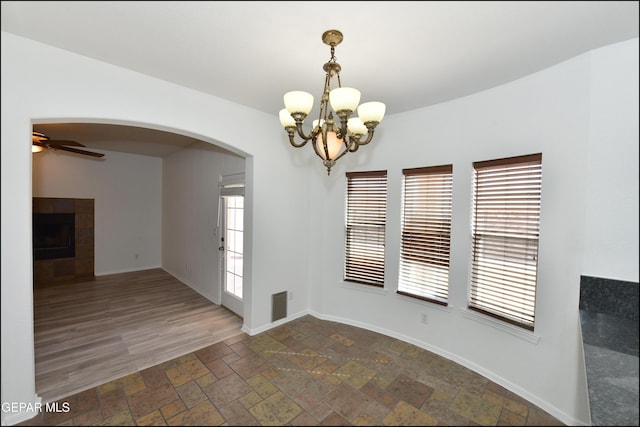 unfurnished dining area featuring a fireplace and ceiling fan with notable chandelier