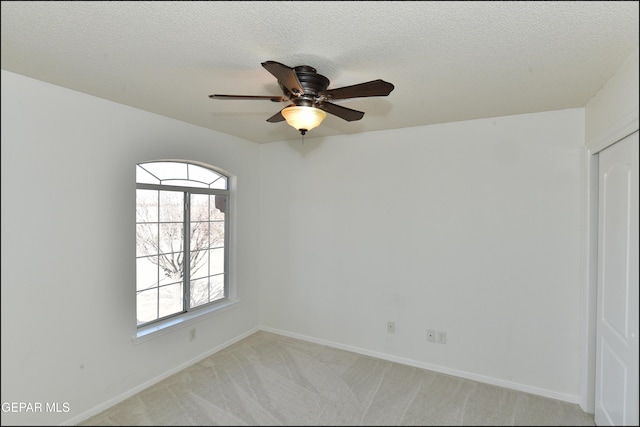 empty room featuring ceiling fan, light colored carpet, and a textured ceiling