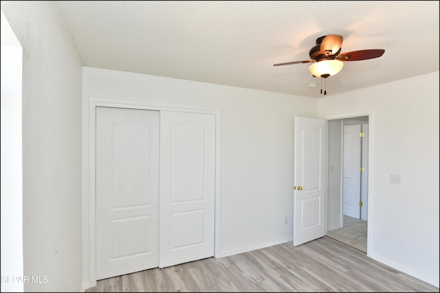 unfurnished bedroom featuring ceiling fan, a textured ceiling, a closet, and light wood-type flooring