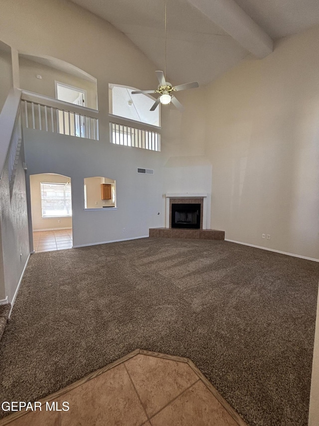 unfurnished living room featuring a tile fireplace, ceiling fan, beam ceiling, high vaulted ceiling, and carpet flooring