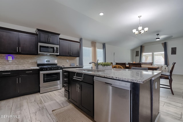 kitchen with lofted ceiling, sink, hanging light fixtures, appliances with stainless steel finishes, and an island with sink