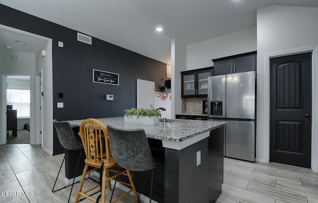 kitchen featuring sink, a breakfast bar, backsplash, stainless steel refrigerator with ice dispenser, and a center island with sink