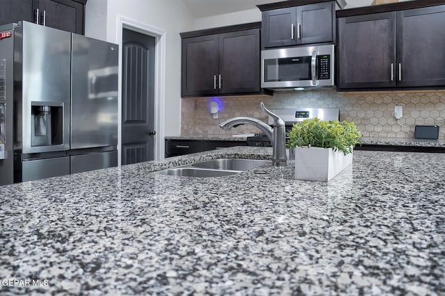 kitchen featuring dark brown cabinetry, sink, light stone counters, stainless steel appliances, and decorative backsplash