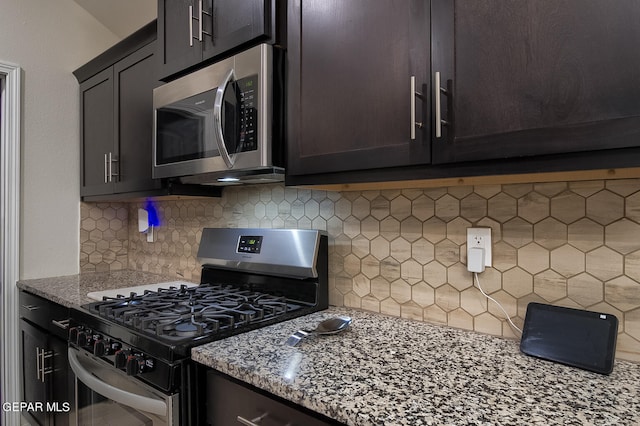 kitchen featuring tasteful backsplash, light stone counters, dark brown cabinetry, and appliances with stainless steel finishes