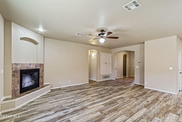 unfurnished living room featuring a textured ceiling, a fireplace, ceiling fan, and light wood-type flooring