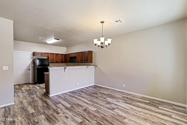 kitchen featuring a breakfast bar area, hanging light fixtures, wood-type flooring, black appliances, and kitchen peninsula