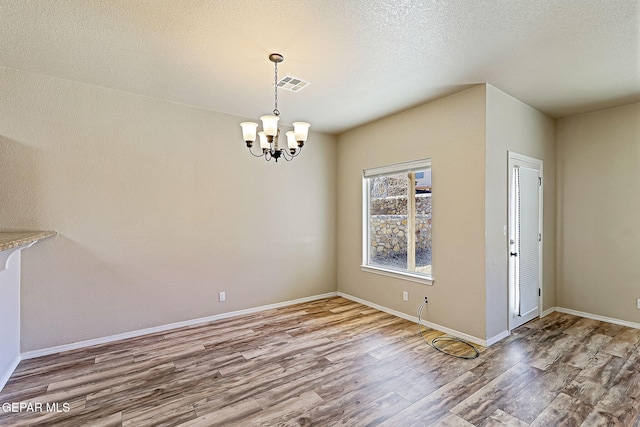 unfurnished dining area with hardwood / wood-style flooring, an inviting chandelier, and a textured ceiling