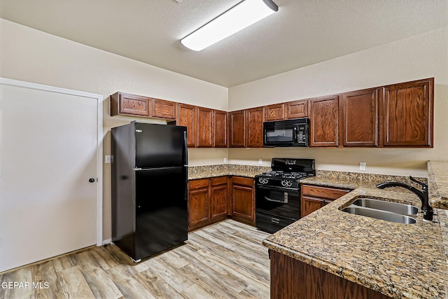 kitchen with sink, dark stone countertops, light hardwood / wood-style floors, black appliances, and a textured ceiling