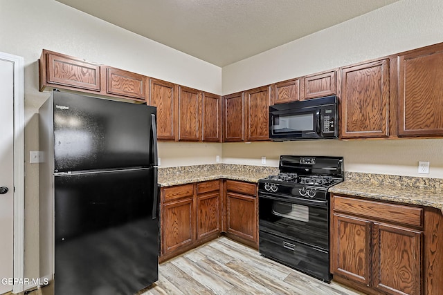 kitchen with light stone countertops, light hardwood / wood-style floors, and black appliances