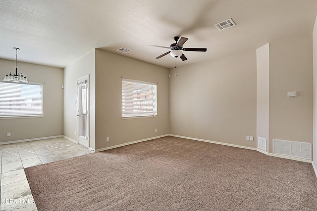 empty room with ceiling fan with notable chandelier, a healthy amount of sunlight, light carpet, and a textured ceiling