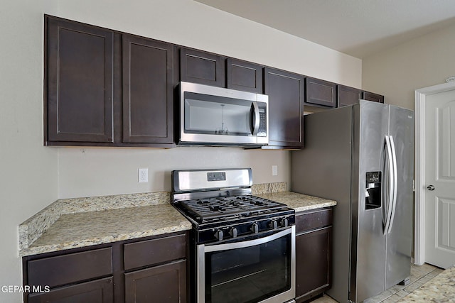 kitchen featuring stainless steel appliances, dark brown cabinets, and light stone counters