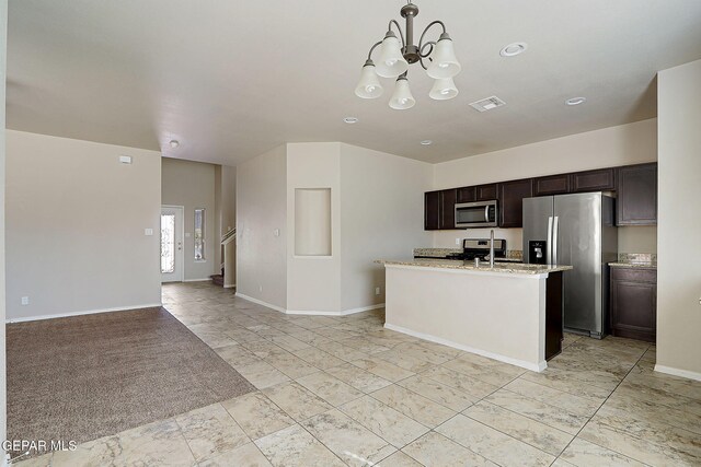 kitchen featuring dark brown cabinetry, light stone counters, decorative light fixtures, appliances with stainless steel finishes, and a kitchen island with sink