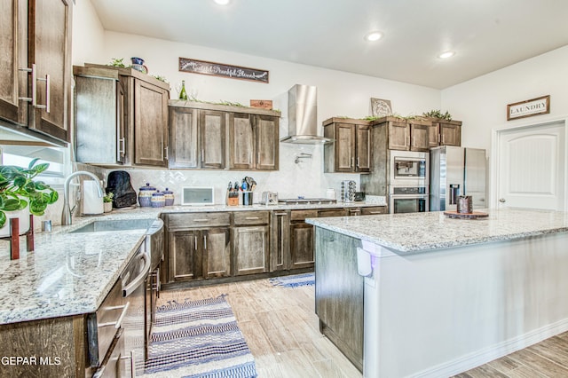 kitchen with wall chimney exhaust hood, light stone counters, a center island, stainless steel appliances, and decorative backsplash