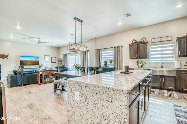 kitchen featuring dark brown cabinetry, sink, light stone counters, a center island, and pendant lighting