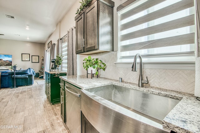 kitchen with stainless steel dishwasher, light stone countertops, sink, and dark brown cabinets