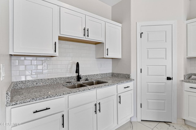 kitchen featuring decorative backsplash, light stone counters, marble finish floor, white cabinetry, and a sink