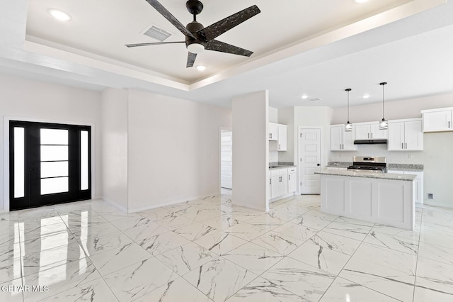 kitchen featuring a raised ceiling, open floor plan, marble finish floor, under cabinet range hood, and stainless steel range oven