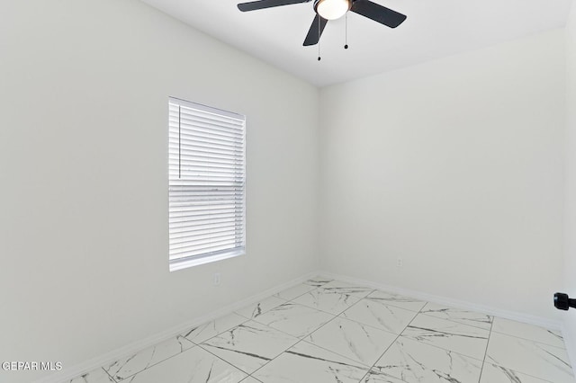 spare room with ceiling fan, marble finish floor, and baseboards