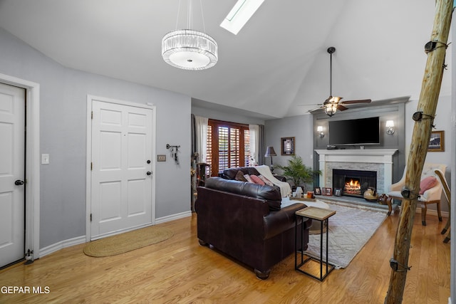 living room featuring lofted ceiling with skylight, ceiling fan, a fireplace, and light hardwood / wood-style floors