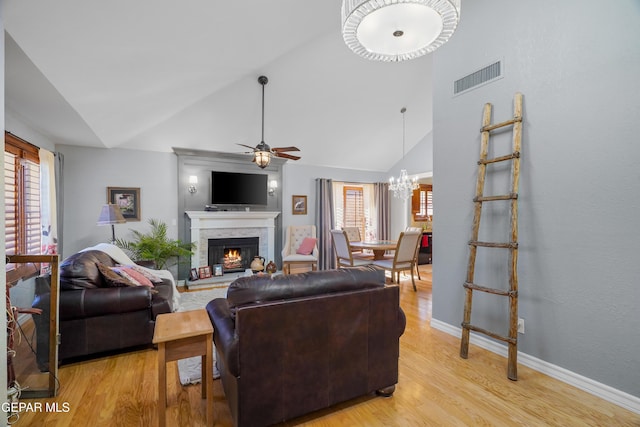 living room featuring high vaulted ceiling, ceiling fan with notable chandelier, a fireplace, and light hardwood / wood-style floors