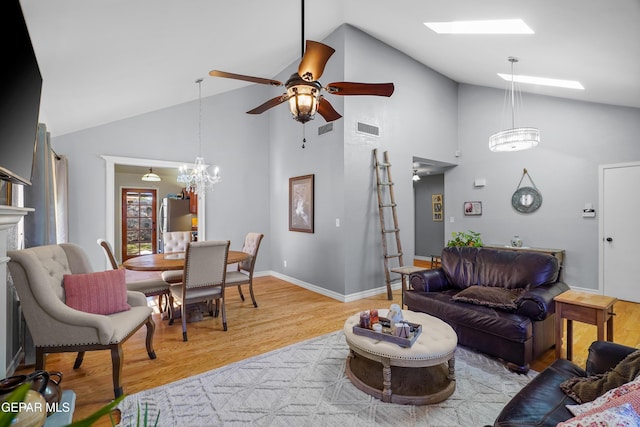 living room featuring ceiling fan with notable chandelier, lofted ceiling with skylight, and light wood-type flooring