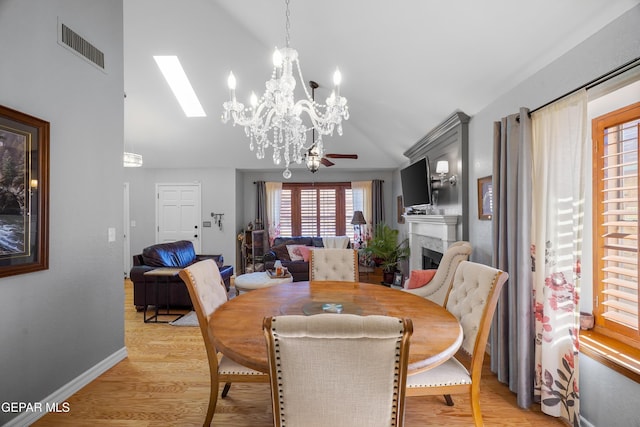 dining area with ceiling fan, a fireplace, light hardwood / wood-style flooring, and lofted ceiling with skylight