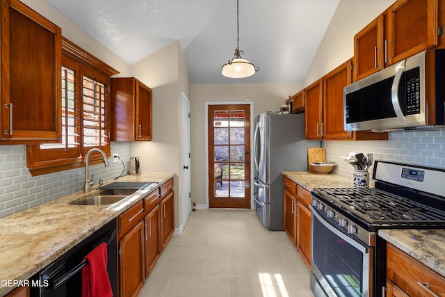 kitchen featuring pendant lighting, sink, appliances with stainless steel finishes, light stone counters, and vaulted ceiling