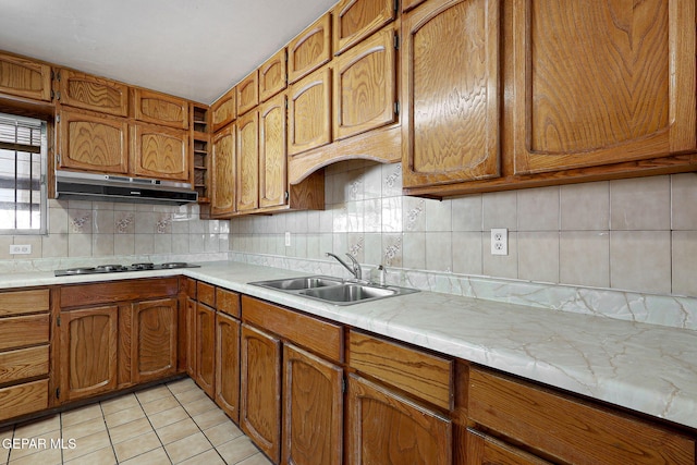 kitchen with light tile patterned floors, under cabinet range hood, a sink, light countertops, and brown cabinetry