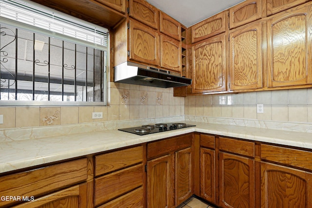 kitchen with light countertops, brown cabinets, black electric cooktop, and under cabinet range hood