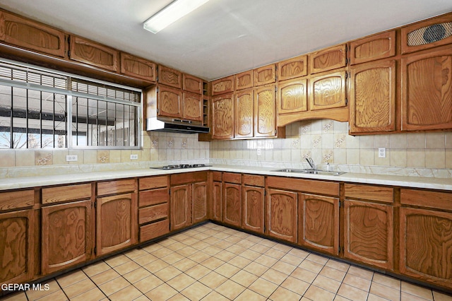 kitchen featuring brown cabinetry, under cabinet range hood, light countertops, and a sink