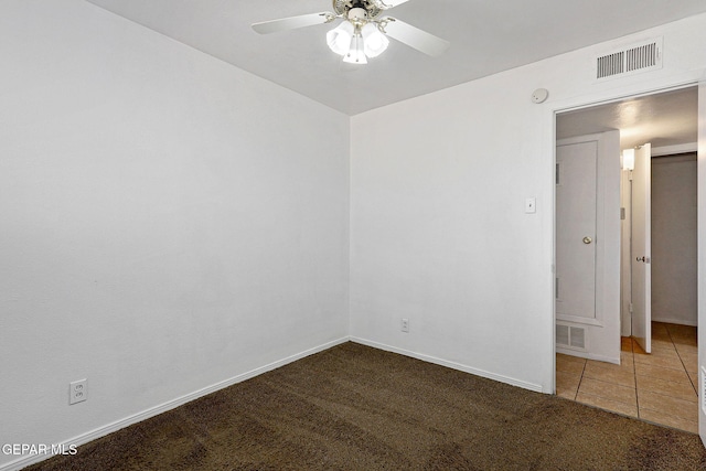 spare room with visible vents, dark carpet, a ceiling fan, and dark tile patterned flooring