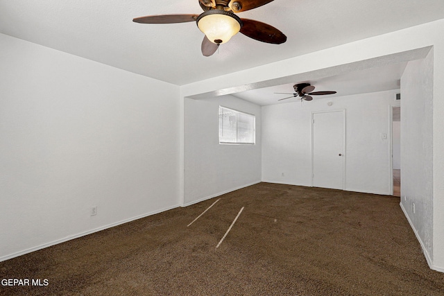 spare room with a ceiling fan, dark colored carpet, and baseboards