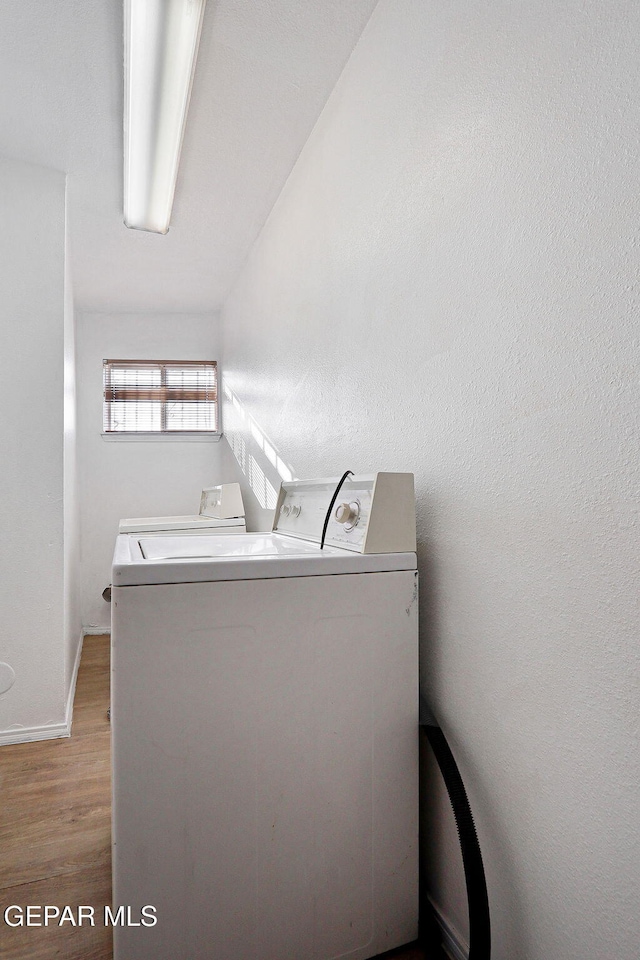 washroom featuring laundry area, baseboards, light wood finished floors, and washing machine and clothes dryer