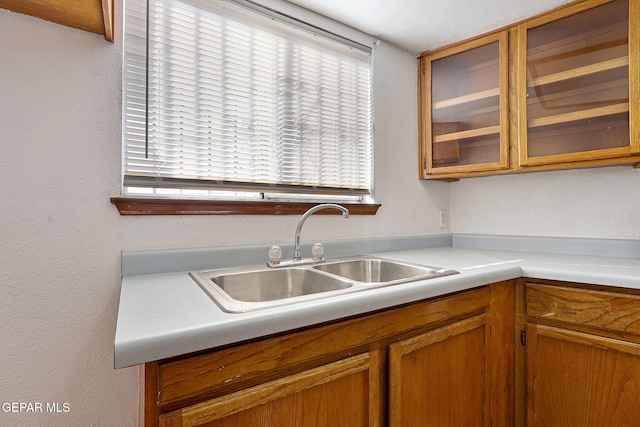 kitchen featuring brown cabinetry, glass insert cabinets, light countertops, and a sink