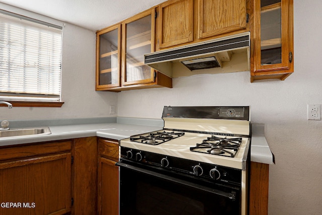 kitchen featuring gas range, glass insert cabinets, light countertops, under cabinet range hood, and a sink