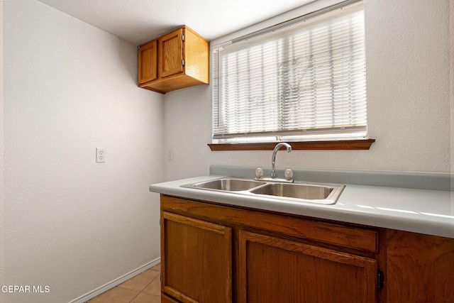 kitchen featuring brown cabinets, light tile patterned floors, light countertops, a sink, and baseboards