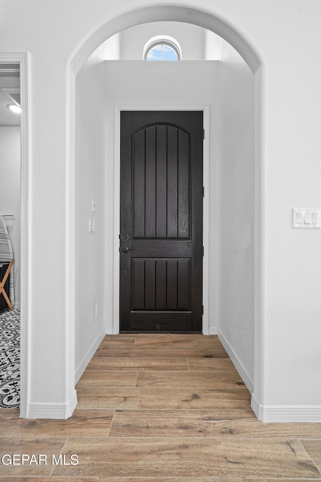 foyer featuring arched walkways, light wood-style flooring, and baseboards