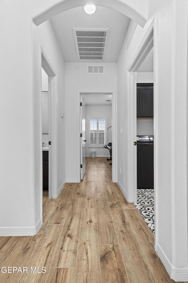 hall featuring arched walkways, visible vents, and light wood finished floors