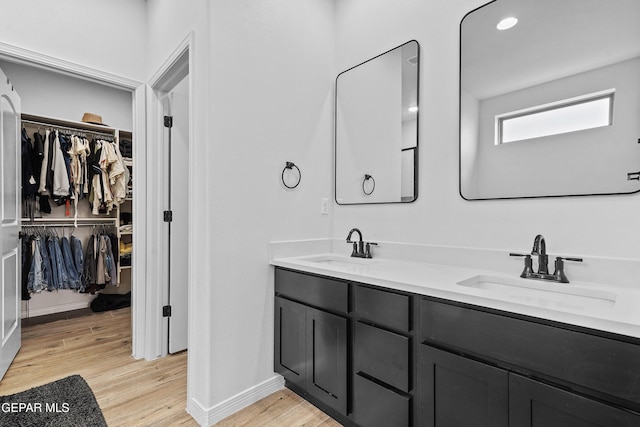 bathroom featuring double vanity, a walk in closet, a sink, and wood finished floors