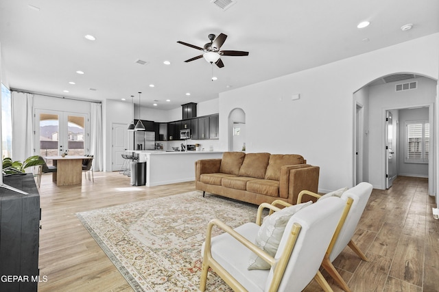 living room with arched walkways, a wealth of natural light, and light wood-style flooring