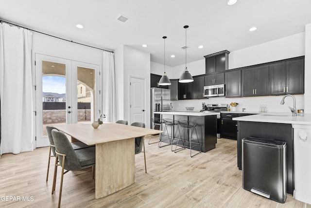 kitchen with stainless steel appliances, light countertops, hanging light fixtures, a sink, and dark cabinetry