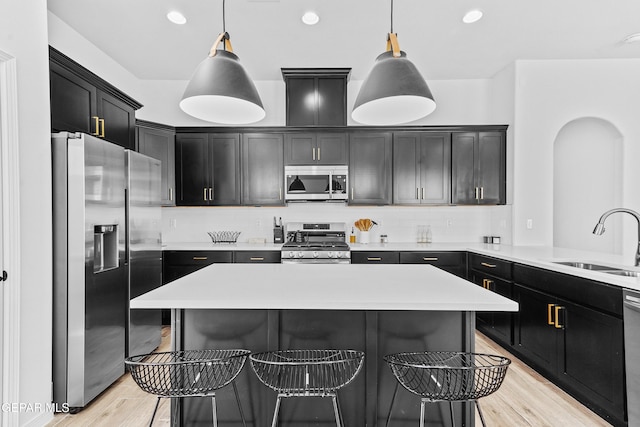 kitchen featuring appliances with stainless steel finishes, a breakfast bar, decorative light fixtures, light countertops, and a sink