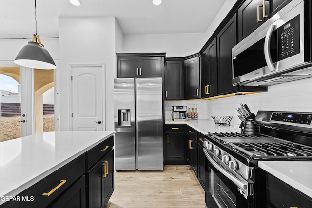 kitchen featuring light countertops, appliances with stainless steel finishes, hanging light fixtures, dark cabinetry, and backsplash