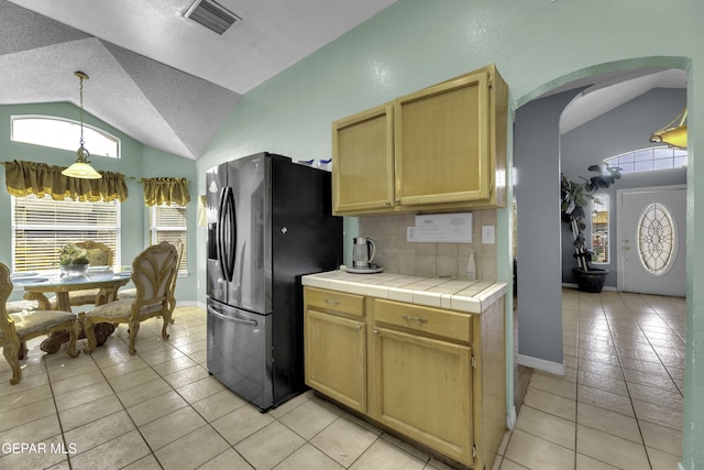 kitchen featuring lofted ceiling, tile countertops, refrigerator with ice dispenser, and decorative backsplash